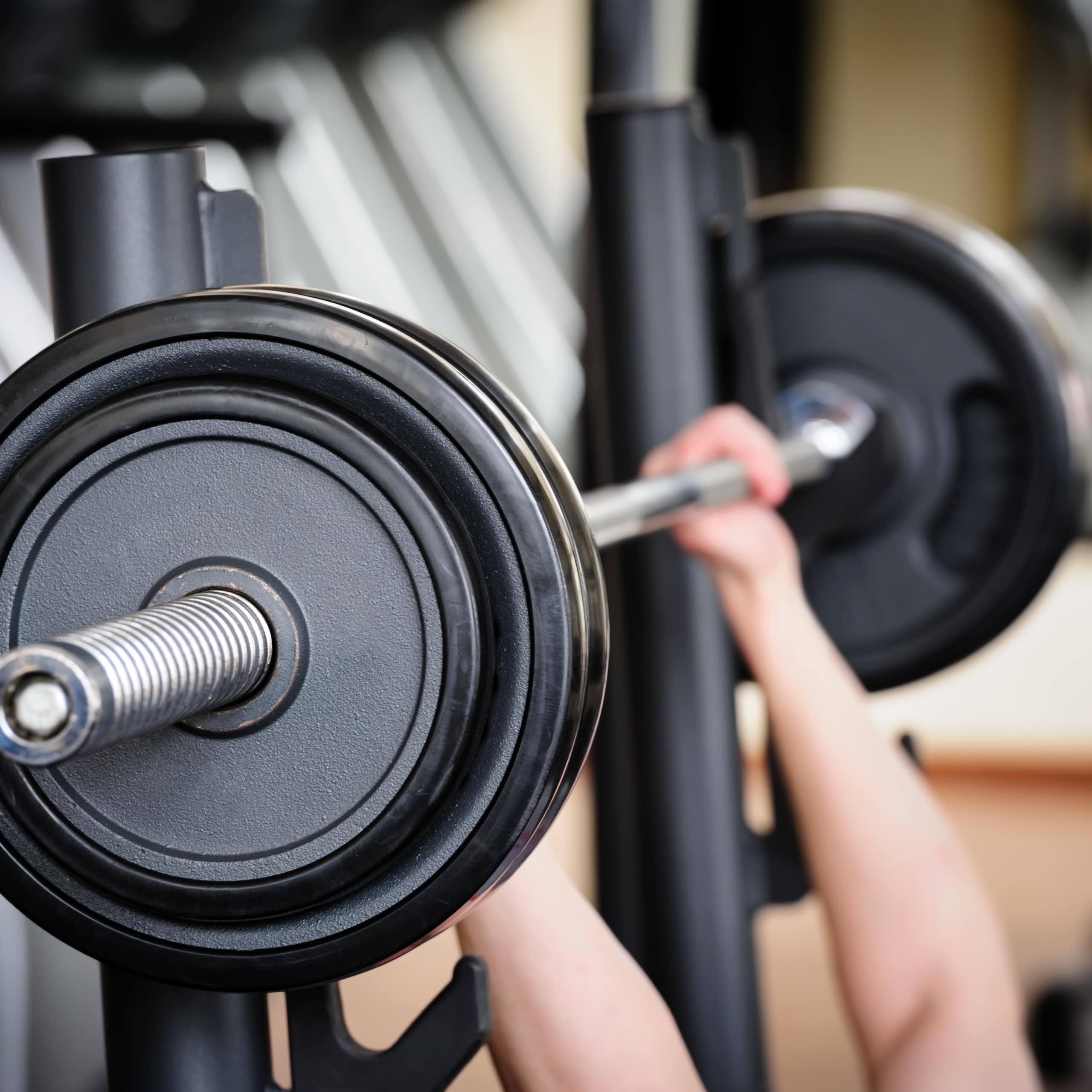 Two hands lift a large barbell in a gym.