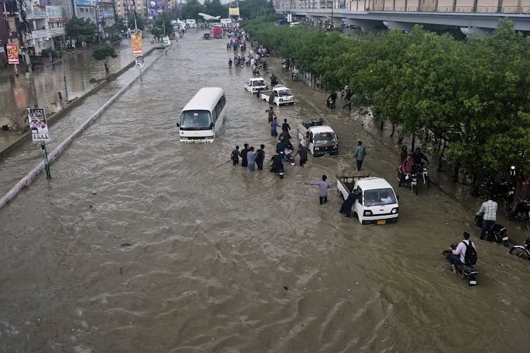 Cars, people and a bus try to move through a flooded street.