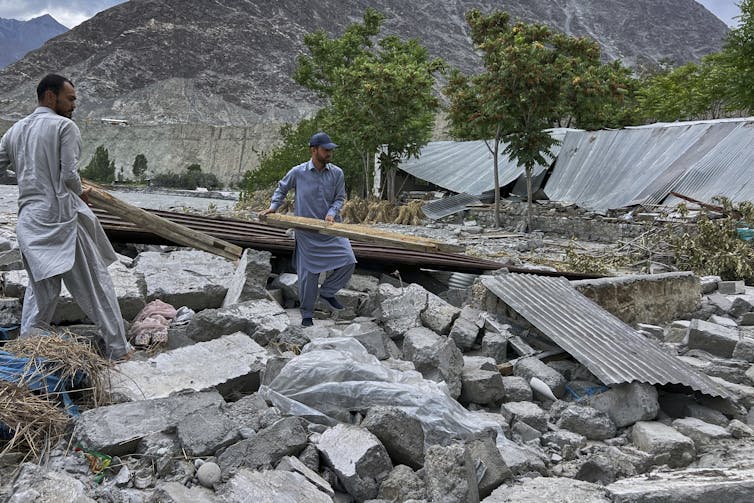 People carry a board as they walk through broken concrete and other debris that once was part of houses.