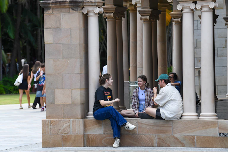 Young people sit against sandstone pillars.