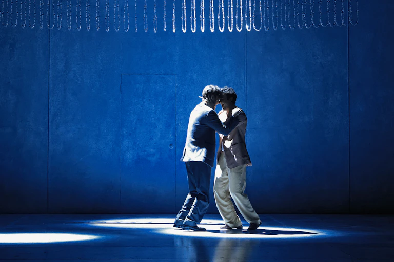 Production image: two men embrace on stage.