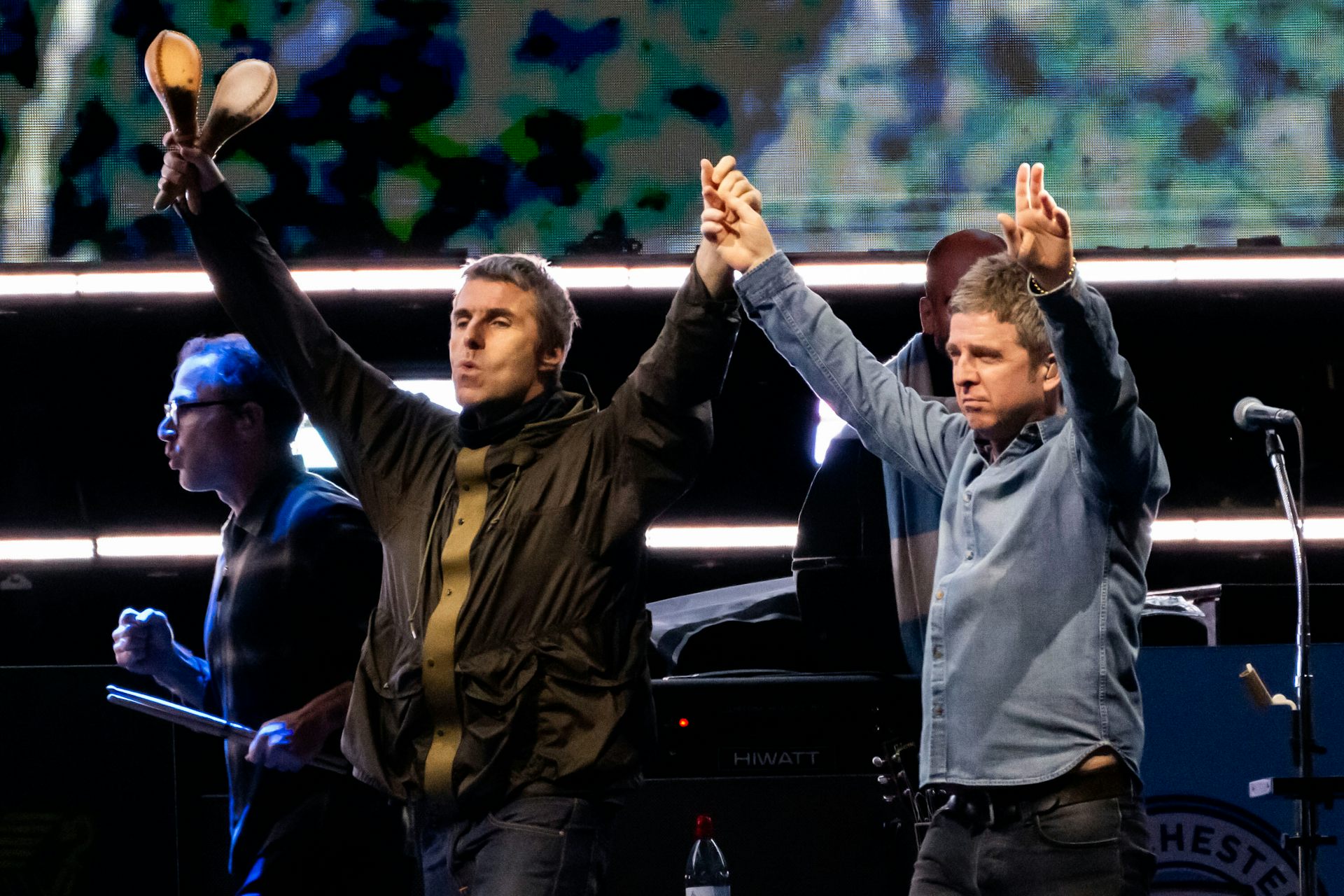 Two dark-haired men hold hands above their hands. One carries a set of maracas.