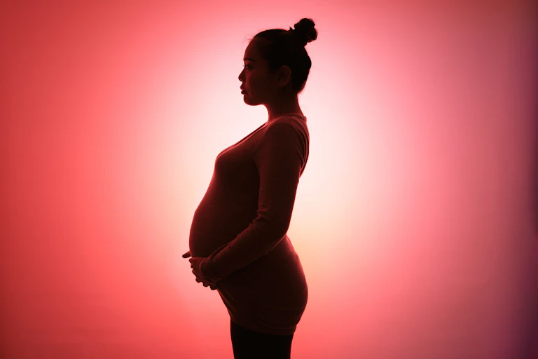 A pregnant woman in silhouette stands against a red and white background.