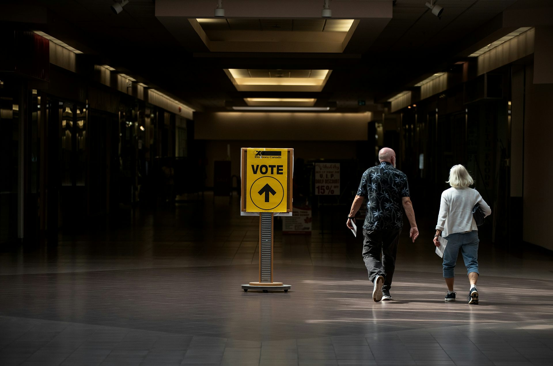 A man and woman walk towards a yellow 'vote' sign.