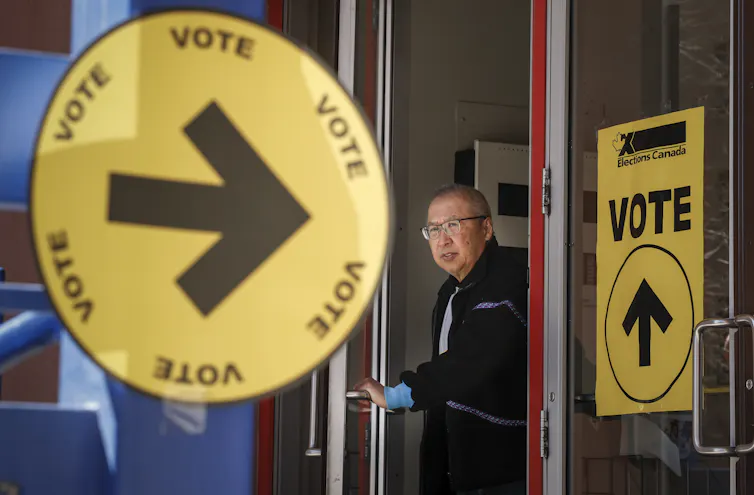 An older person leaves a polling station; a yellow vote sign points toward him.