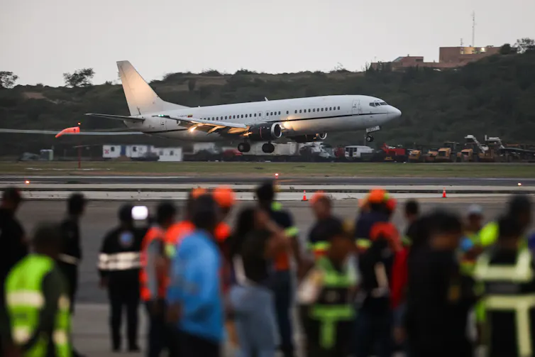 An airplane lands on a runway as people watch in the foreground.