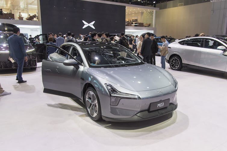 A gray car sits on a showroom floor under bright lights.