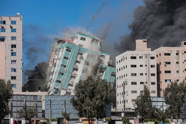 A building is seen toppling to the ground with thick black smoke around it.