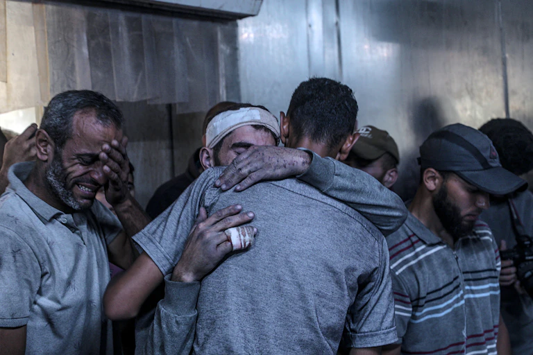 Palestinian men consoling each other after an airstrike.
