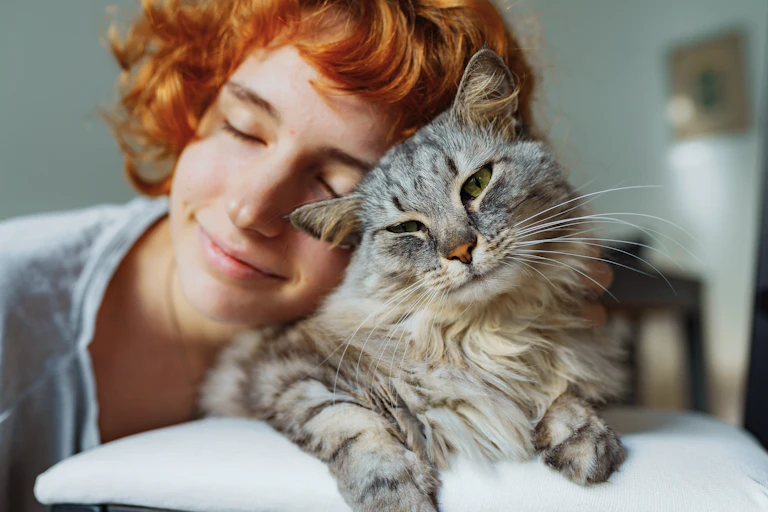 A young woman cuddles with her grey tabby cat.