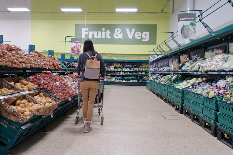 female shopper browses the fruit and vegetable aisle with a trolley in a uk supermarket