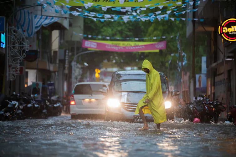 A man in a yellow rain coat walking across a flooded street.
