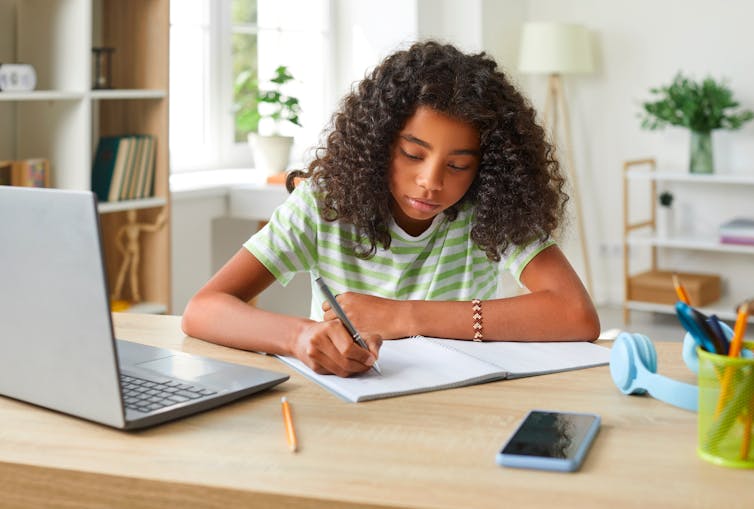 Girl doing homework with pen, paper and laptop