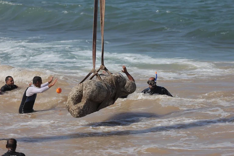 Divers with a statue that is being hoisted from the ocean