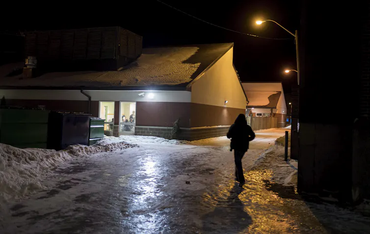 La persona camina hacia un edificio ardiente en la oscuridad. La nieve está en el campo junto al camino.