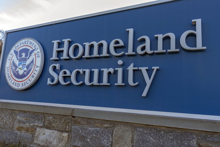 A large outdoor sign with a round logo and text mounted on a stone base.