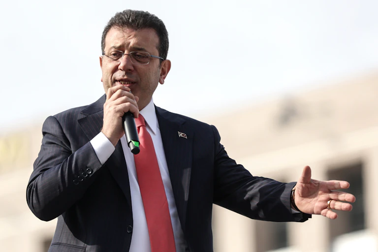 Man in suit and red tie speaks into a microphone