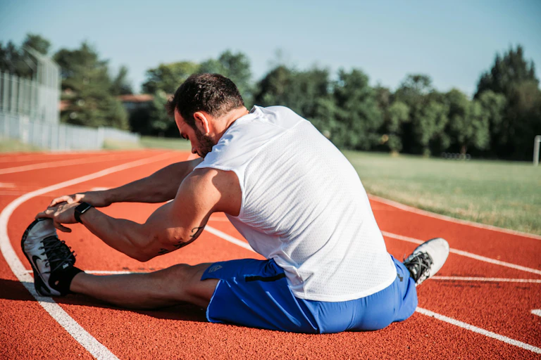 Man in shorts and singlet stretches on running track.