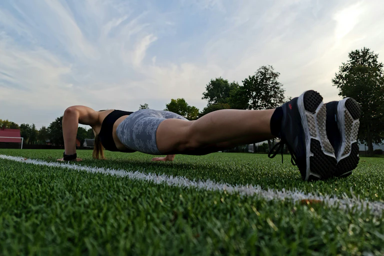 A woman is seen doing push-ups at a soccer field.