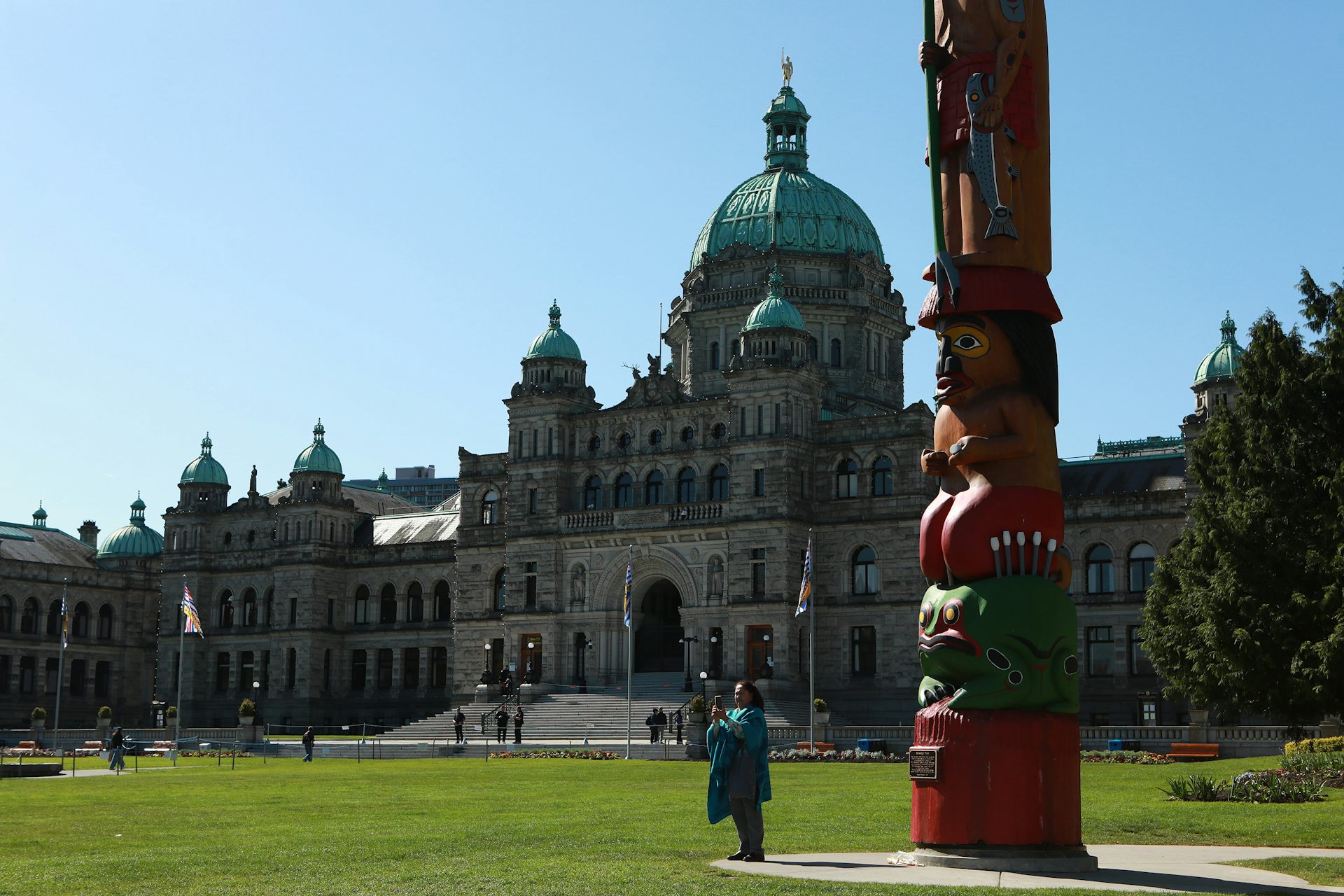 A totem pole on a lawn in front of a large european style building with a dome