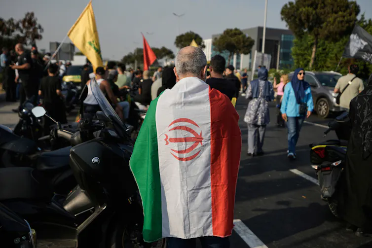 What is the Islamic Revolutionary Guard Corps, or the IRGC? 1 A man stands with his back to the camera draped in an Iranian flag