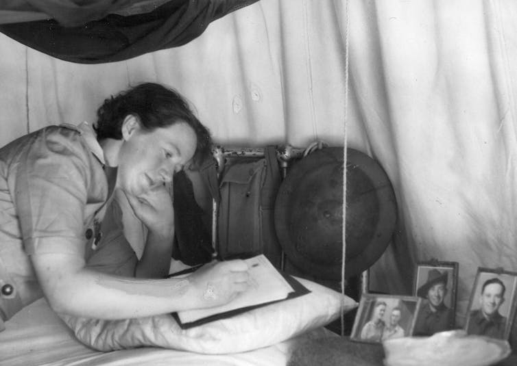 A woman writes in a tent, three photos nearby.