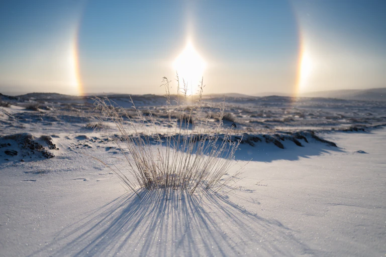Two bright lights appear either side of the Sun above a snow field.