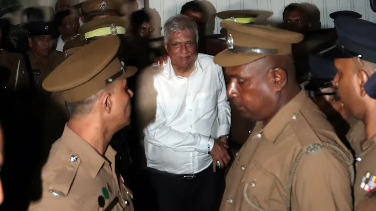 Prison officers escorting a handcuffed Ranil Wickremesinghe.