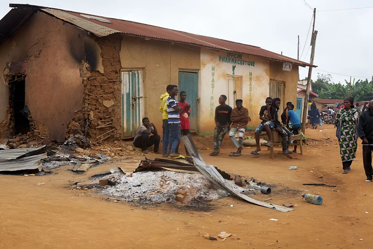 Pile of ashes outside a damaged building; people standing around