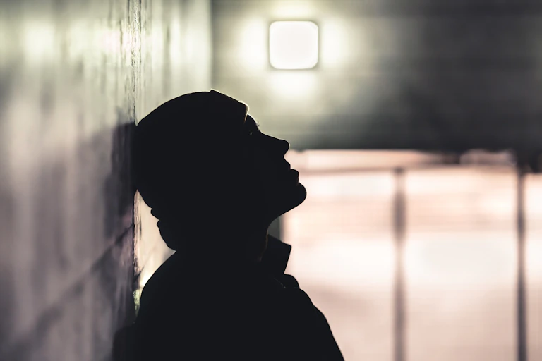 Silhouetted man leas head back against wall