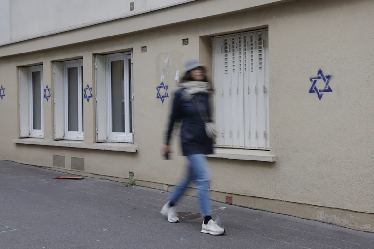 Une femme marche devant des tags représentant des étoiles de David bleues sur une façade d'immeuble.
