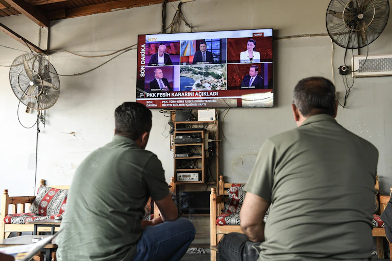 Two men sit watching a TV at a cafe.
