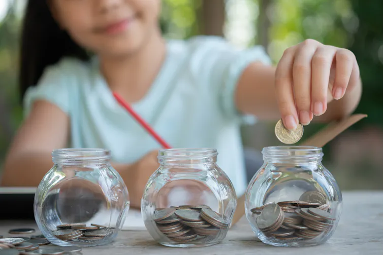 Une petite fille mettant de la monnaie dans des tirelires