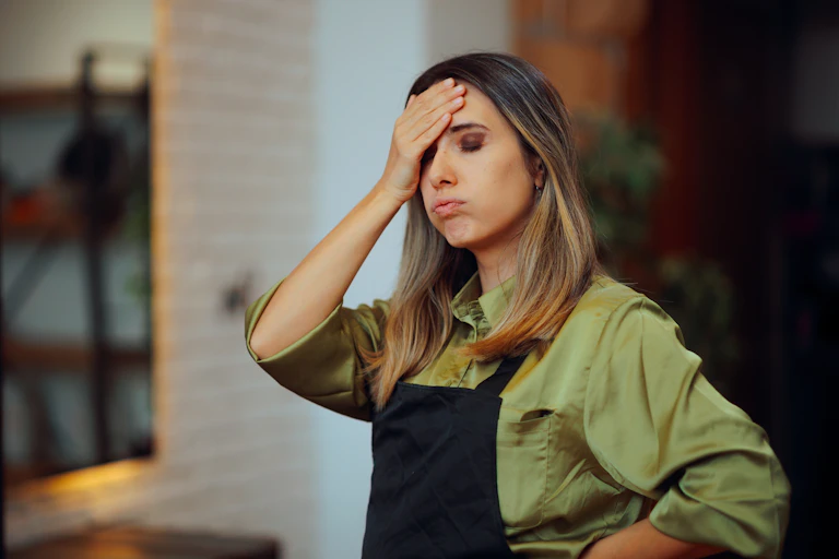 frustrated female worker wearing an apron and rubbing her head