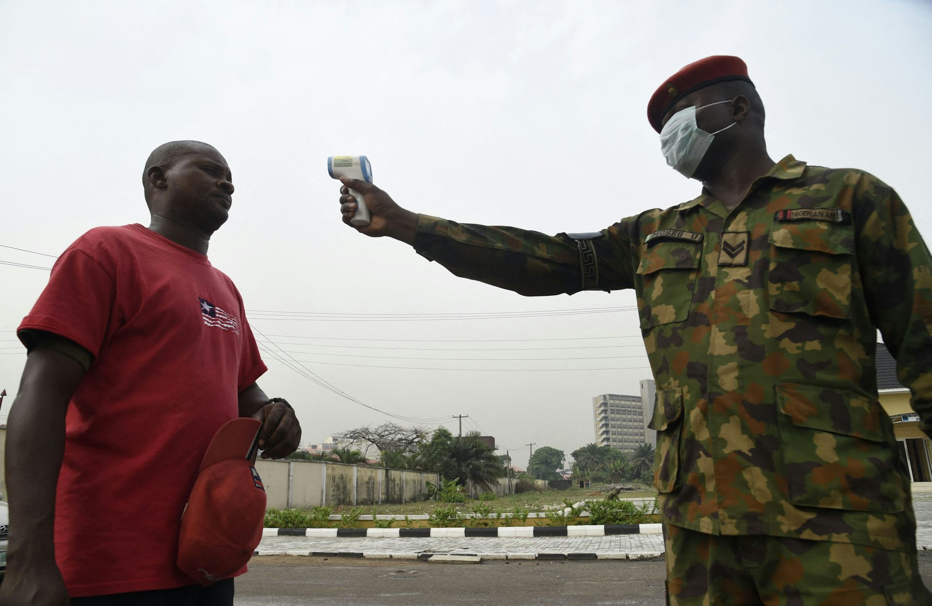 A man in army uniform pointing an infrared thermometer at another man
