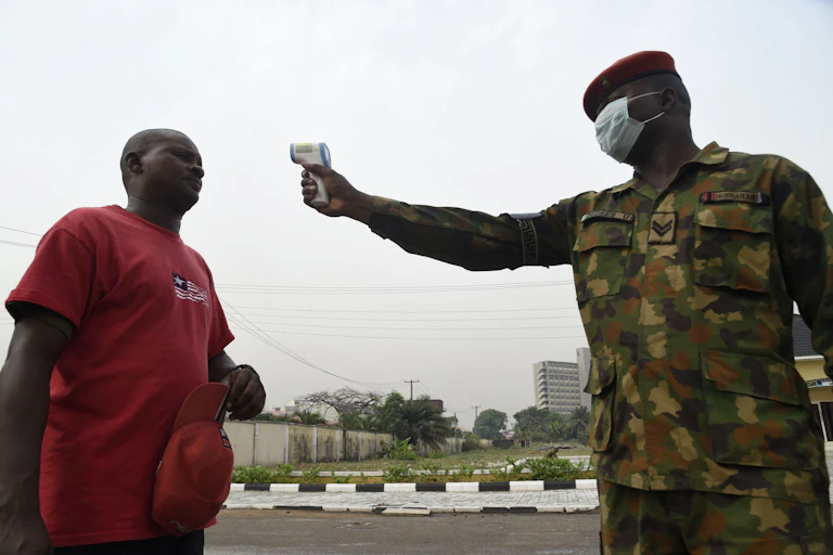 A man in army uniform pointing an infrared thermometer at another man