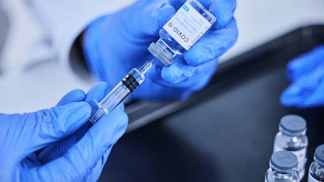 Blue-gloved hand drawing COVID-19 vaccine from a syringe