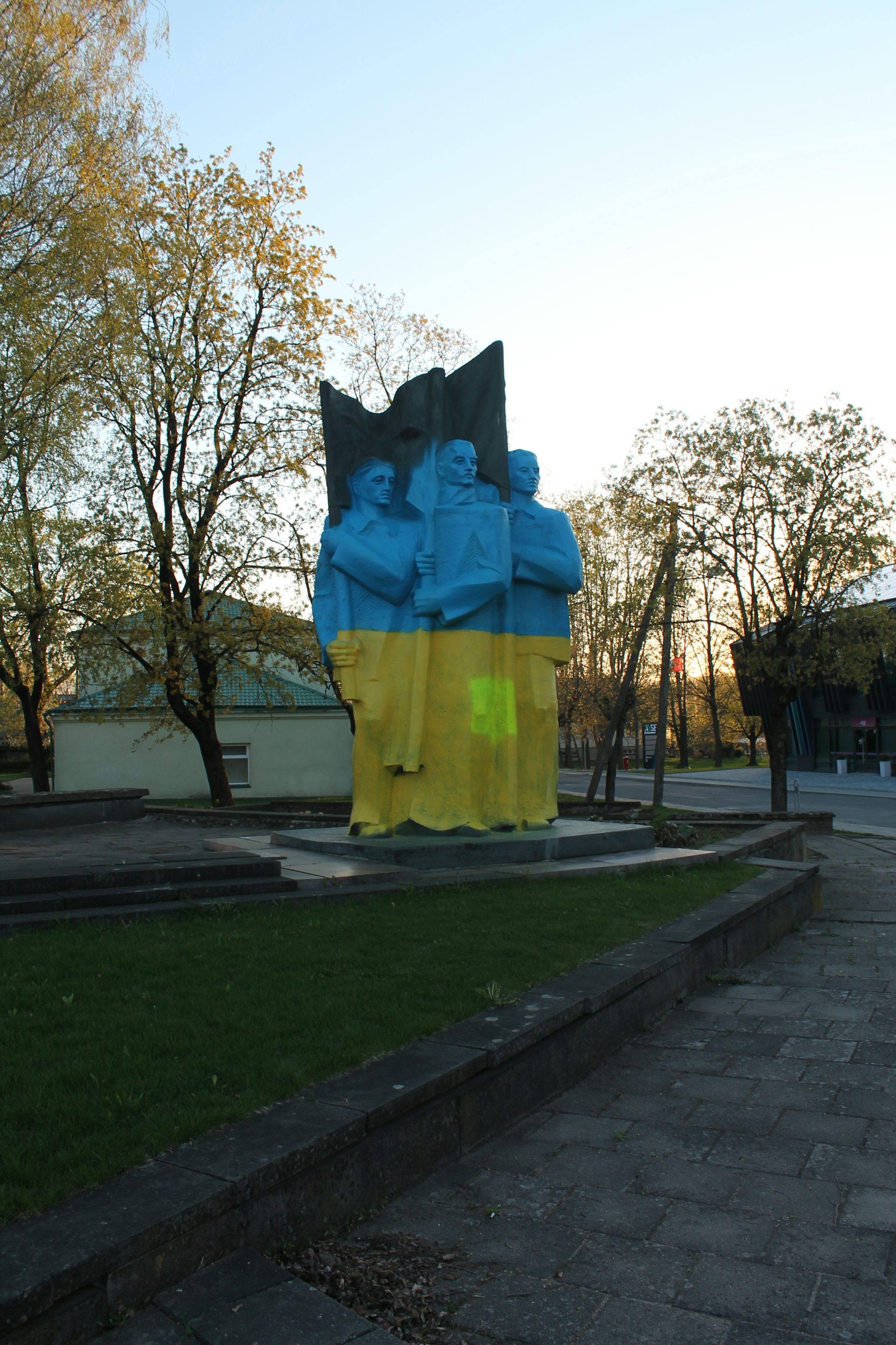 A monument depicting three Soviet-era figures covered in blue and yellow paint.