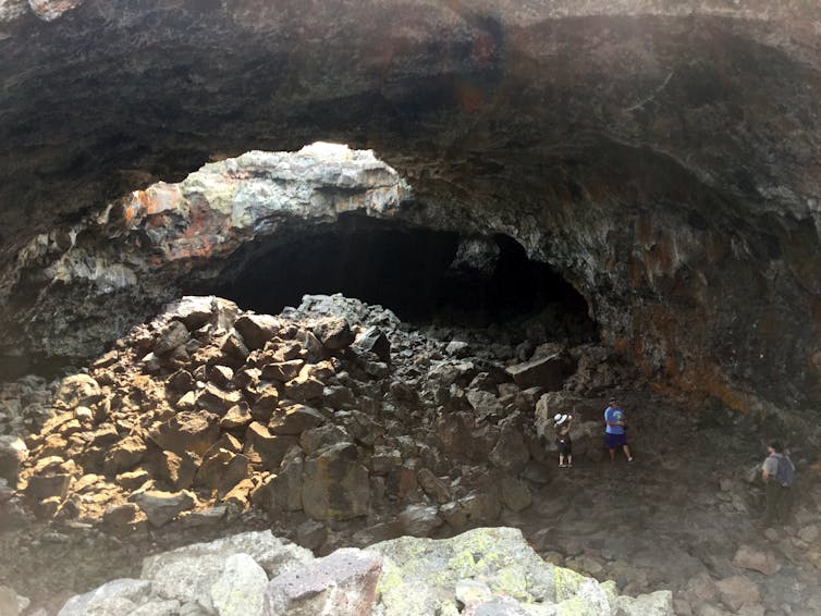 People walk on rocks in a cave, below an opening to the sky.