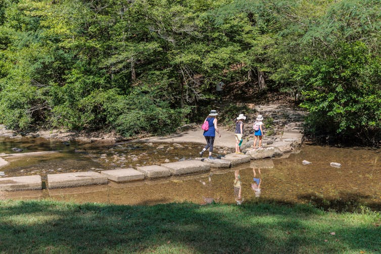 People walk across a stone bridge toward a wooded area.