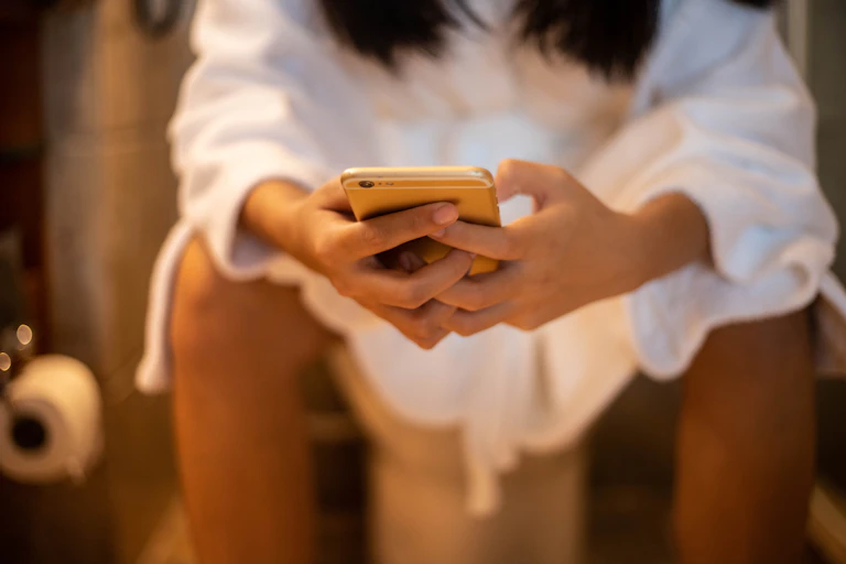Woman sitting on toilet leaning forward hands holding smartphone