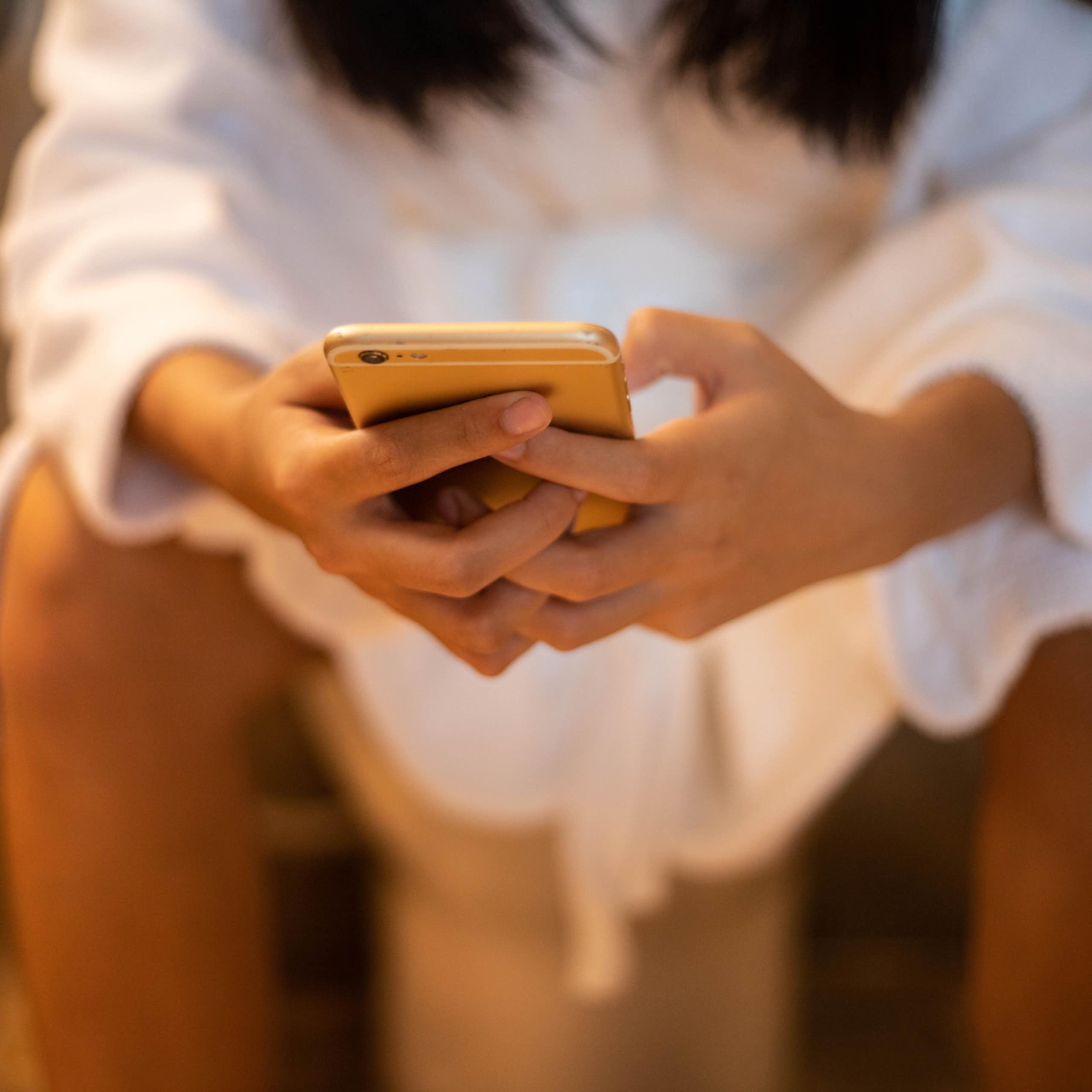 Woman sitting on toilet leaning forward hands holding smartphone