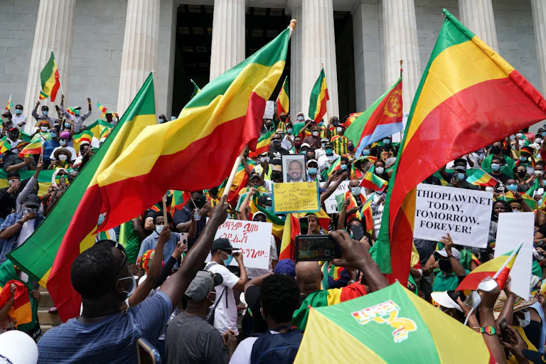 A group of people standing in front of a building, hands raised and waving flags with green, yellow and red stripes