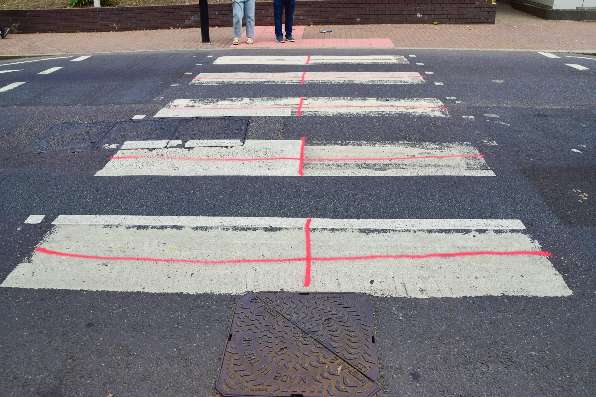 A zebra crossing daubed with red paint so that each white part of the crossing looks like an English flag.
