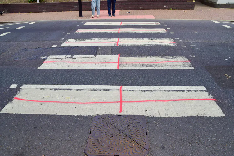 A zebra crossing daubed with red paint so that each white part of the crossing looks like an English flag.