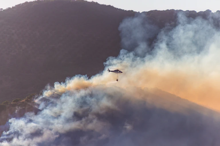 Un helicóptero de extinción sobrevuela una zona cubierta de humo por un incendio