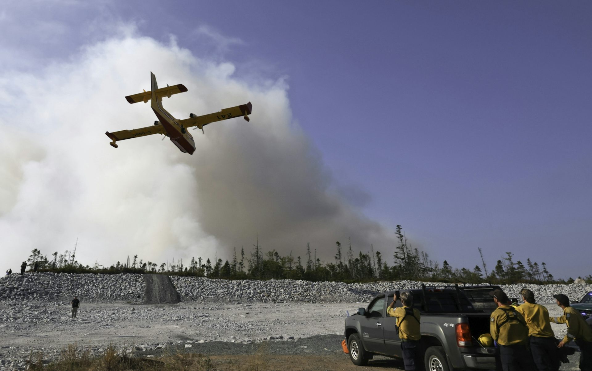 Un avión que vuela hacia la gran fruta de humo blanco, la gente se encuentra al lado del camión cercano