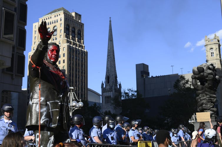 Large bronze statue of man with red paint splashed across his head and chest