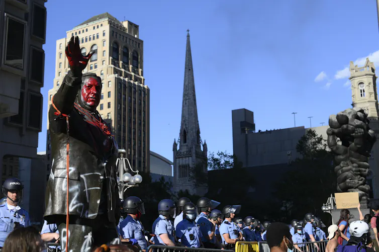 Large bronze statue of man with red paint splashed across his head and chest