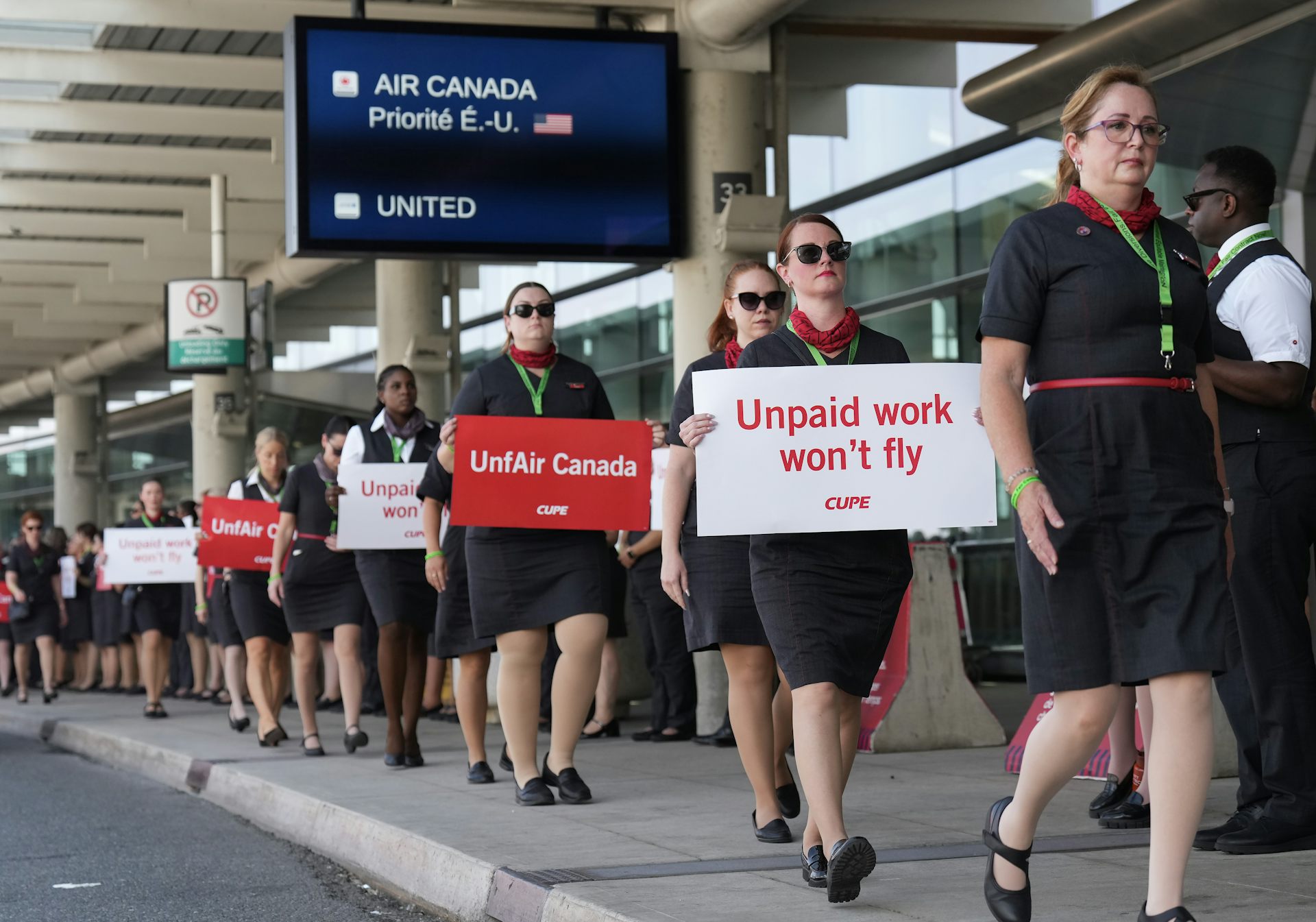 Una fila de mujeres con los uniformes de los asistentes de vuelo que caminan sobre la línea de protesta de sostenimiento que dicen que 